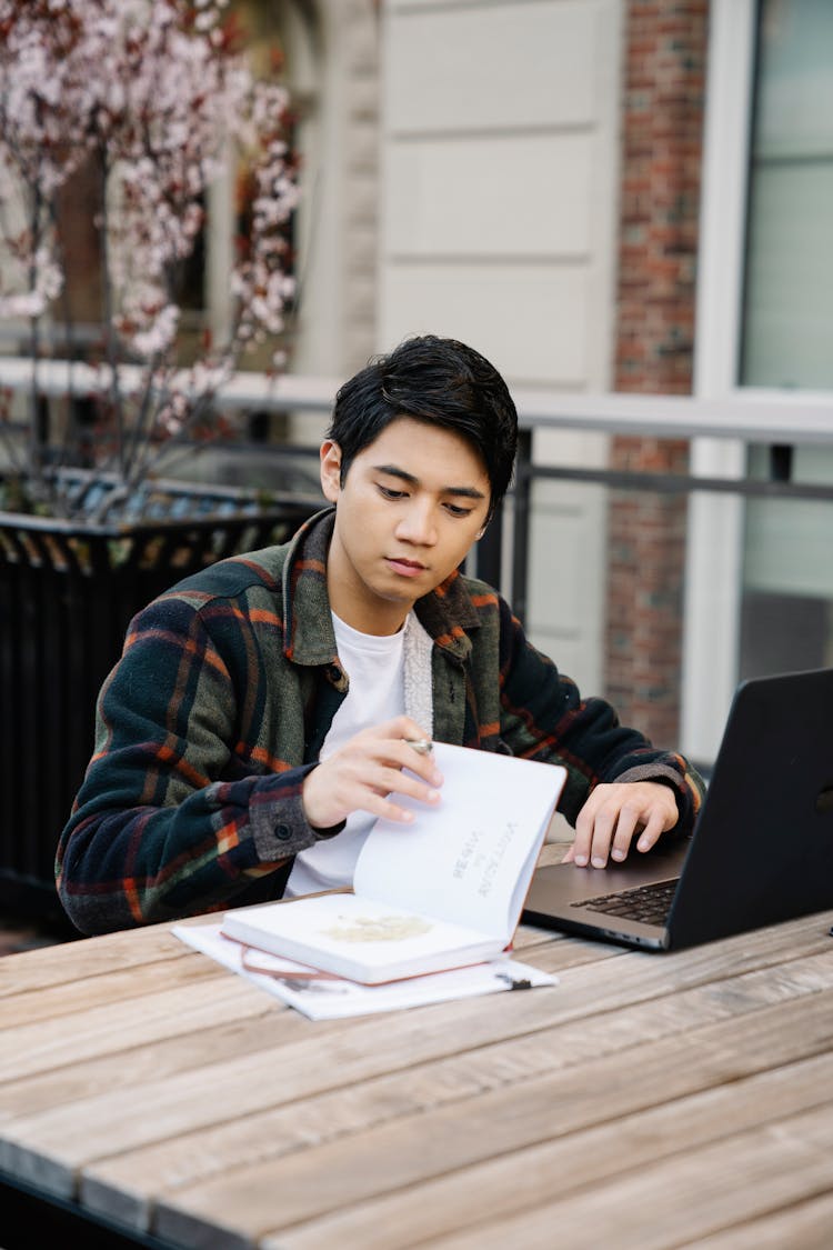 Young Man Studying Outside With A Laptop And Book