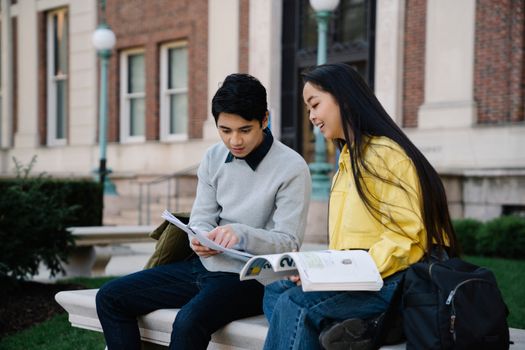 Two students enjoying study time on campus, sitting on a bench and reading books.