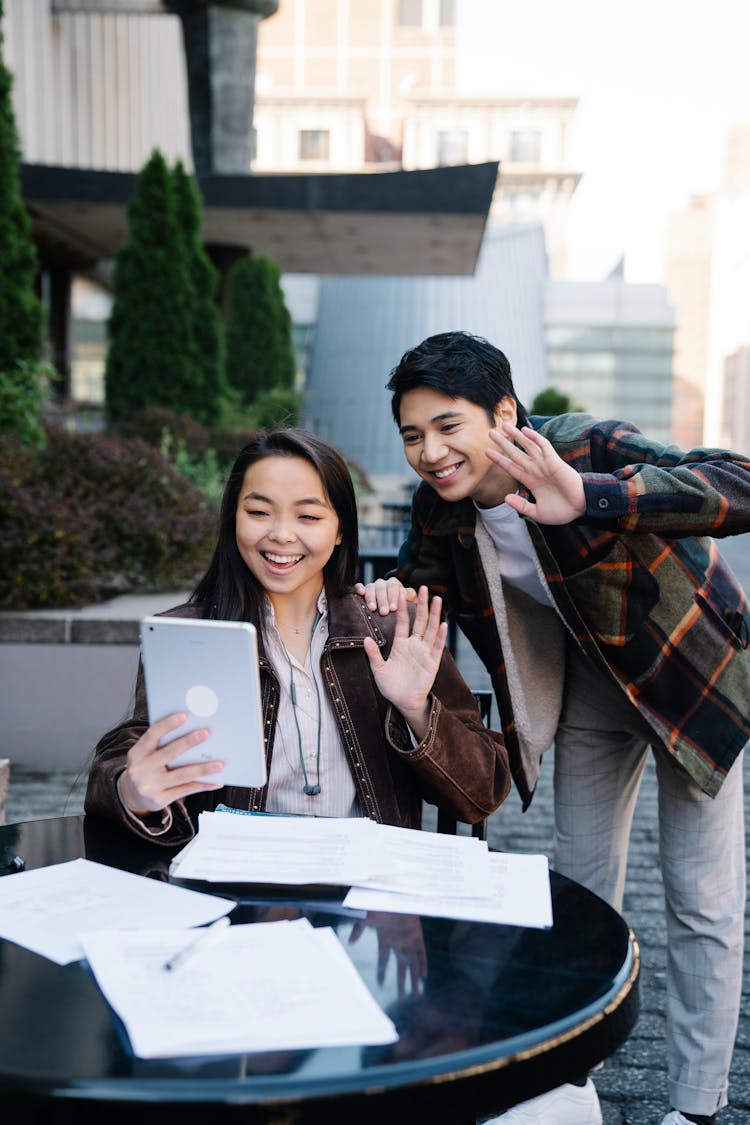 Two Students Waving Cheerfully At Digital Tablet During A Video Call