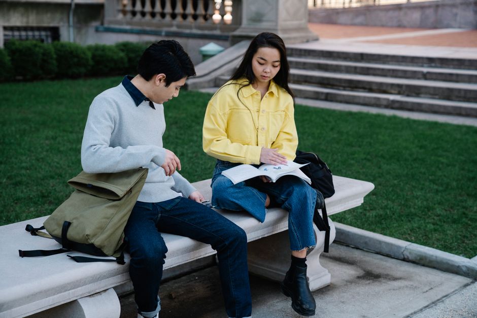 公園の環境でコンクリートのベンチに座り、読書に熱中している二人の大学生。