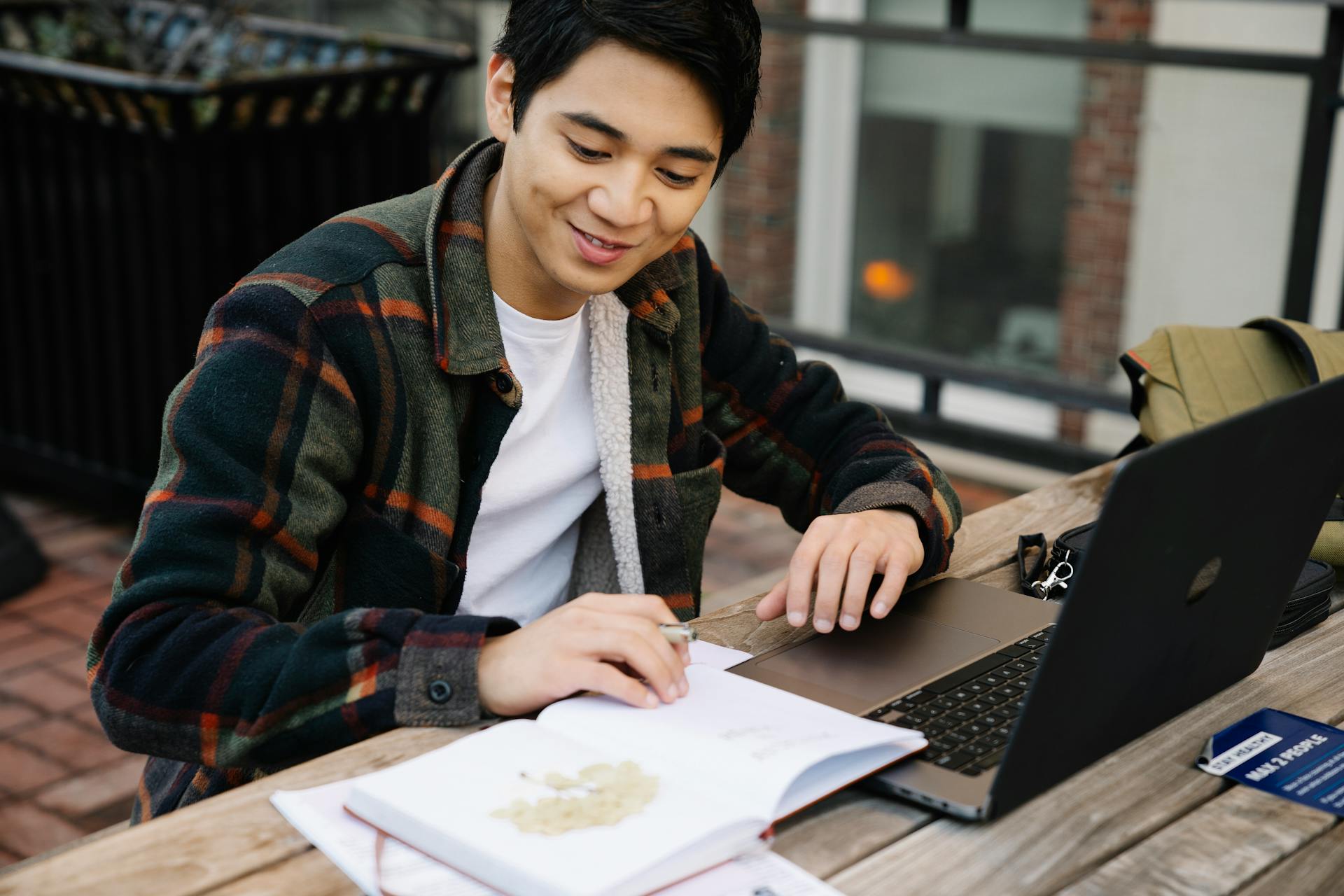 Adult male studying outside using a laptop and a notebook on a wooden table. Education concept.