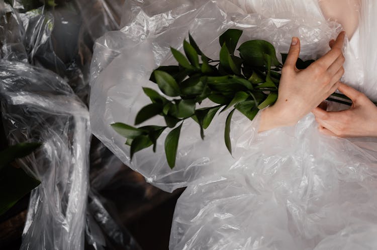 A Person Covered With Plastic Holding Stems Of Green Leaves