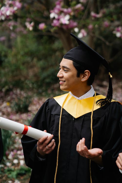 卒業証書を保持しているアカデミックドレスの笑顔の男