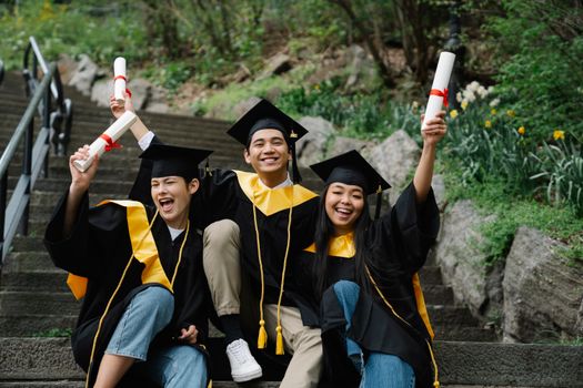 Three happy graduates celebrating on steps with diplomas outdoors.