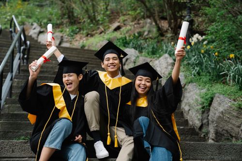 Free Three happy graduates celebrating on steps with diplomas outdoors. Stock Photo