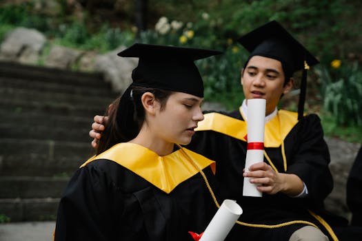 Two young graduates celebrating their achievement with diplomas and caps outdoors.