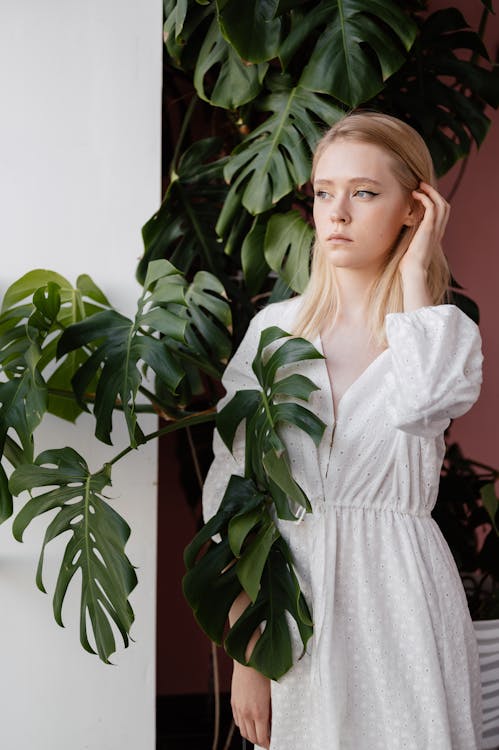 Woman in White Dress Standing Beside A Green Plant Looking Afar