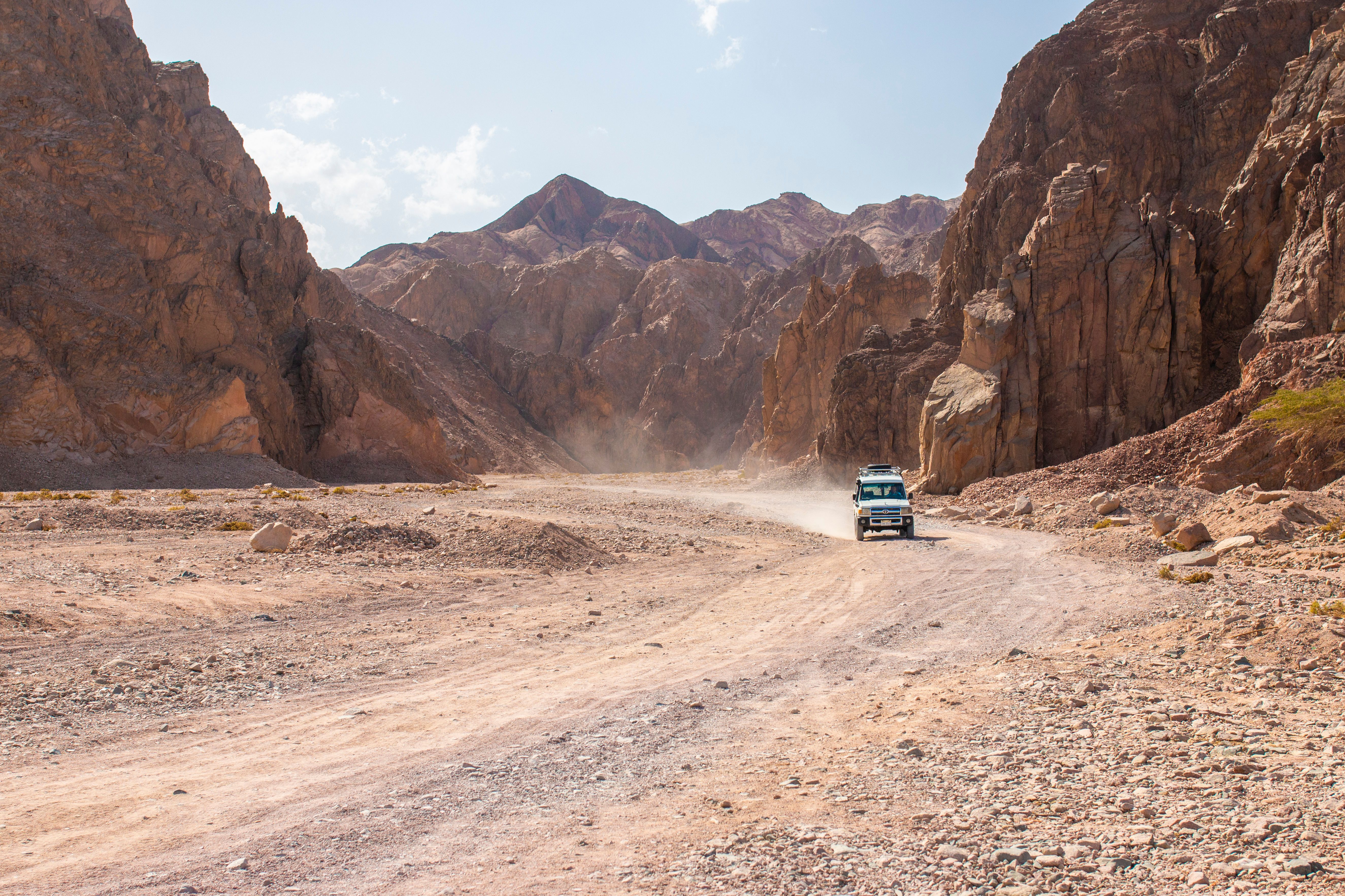 White 4x4 SUV driving a rugged desert canyon dirt road in four-wheel drive
