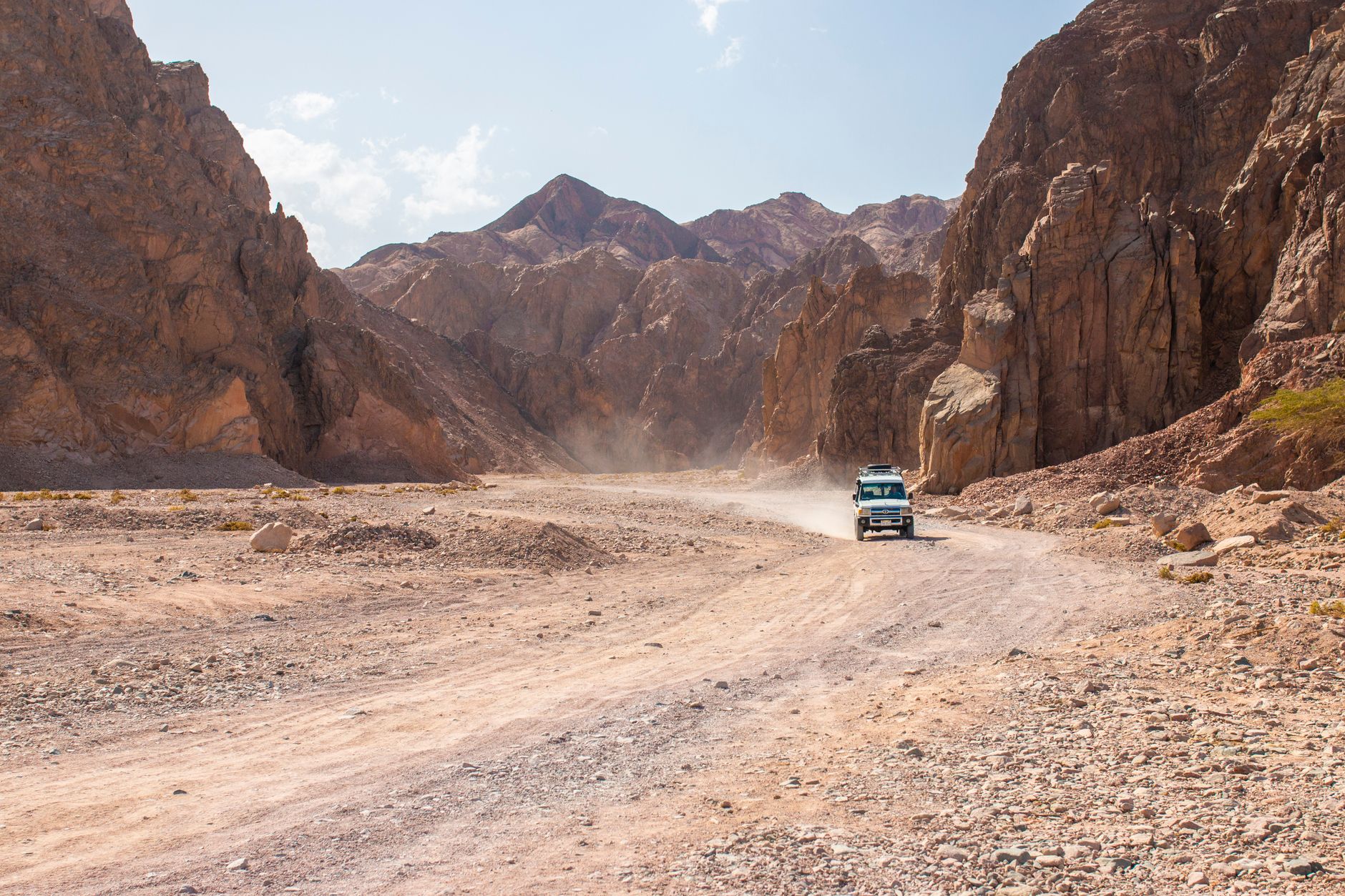 White 4x4 SUV driving a rugged desert canyon dirt road in four-wheel drive