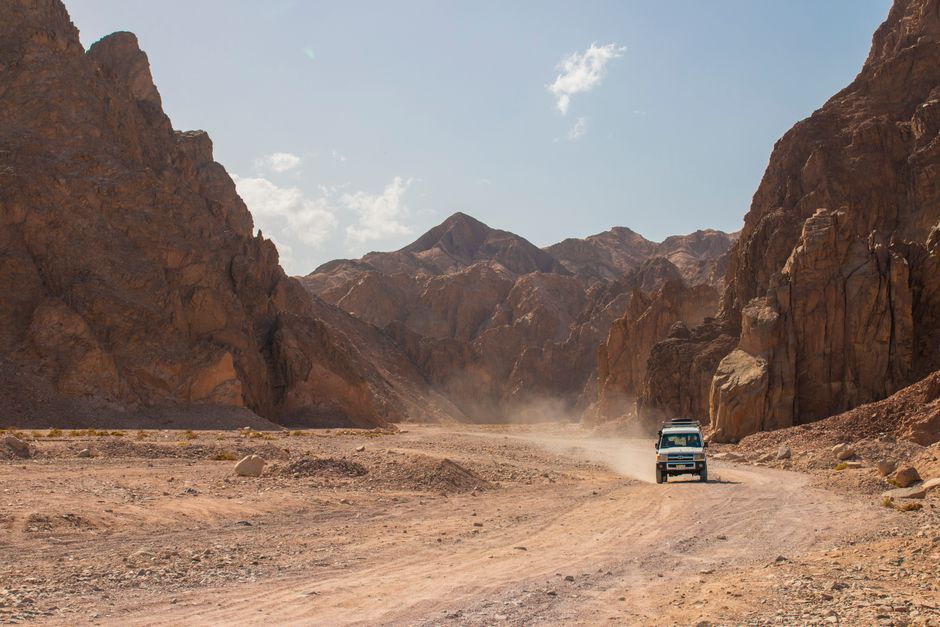 Explore rugged terrains with a jeep driving through a rocky desert canyon under a clear sky.