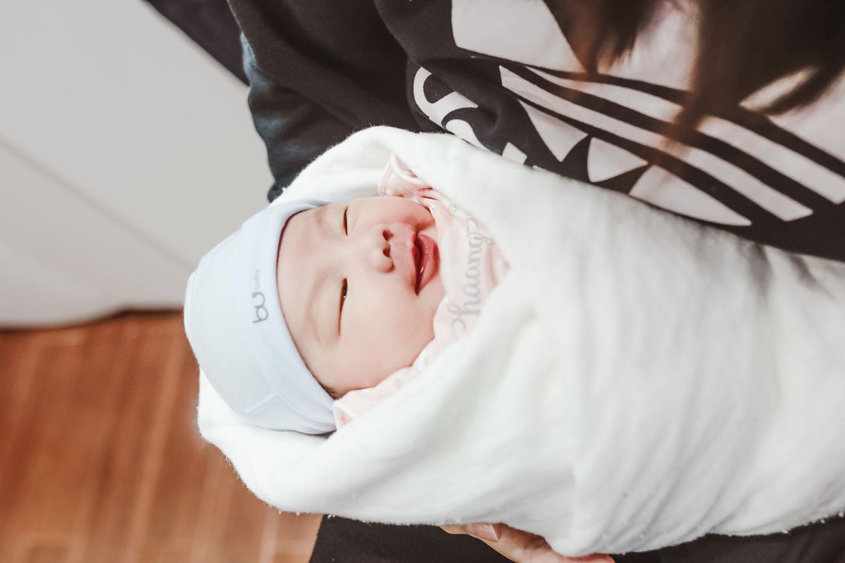 Newborn baby wrapped in a blanket held by a parent for first birthday photoshoot ideas
