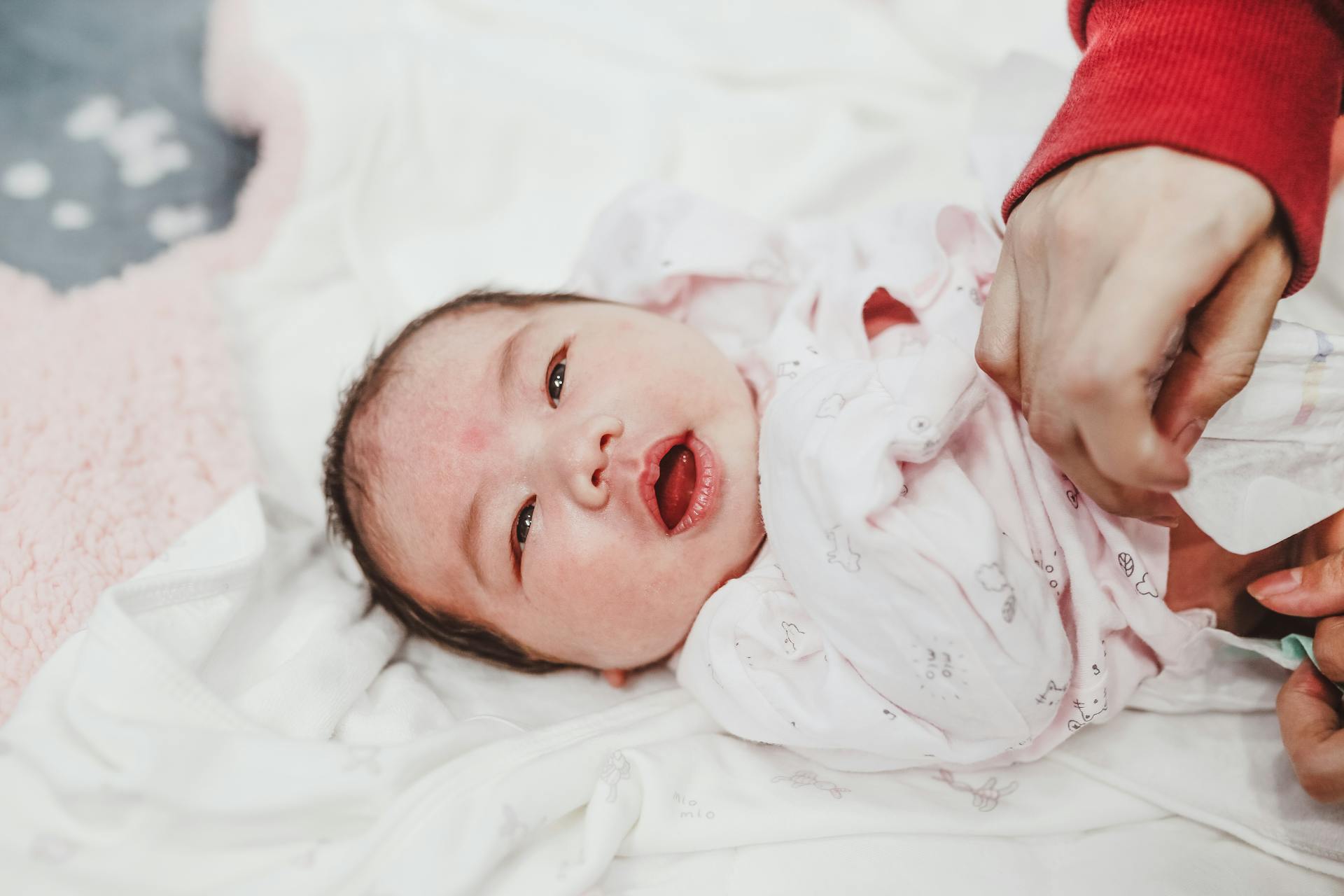 Female hand putting on diaper on adorable newborn child lying on white soft swaddling clothes