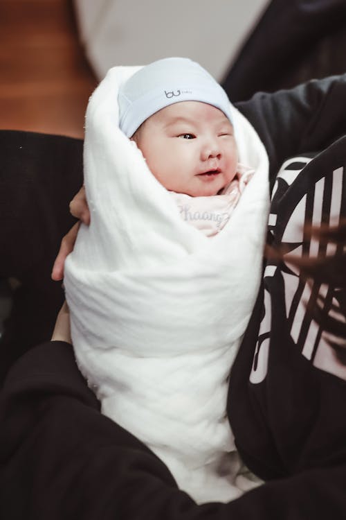 Free Smiling ethnic newborn wrapped in white blanket on hands Stock Photo