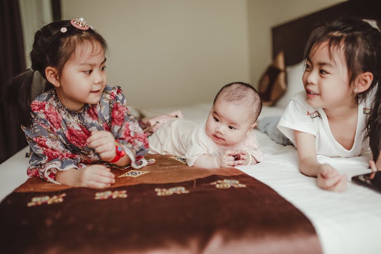 Happy Asian Sisters Having Fun With Newborn Baby On Bed