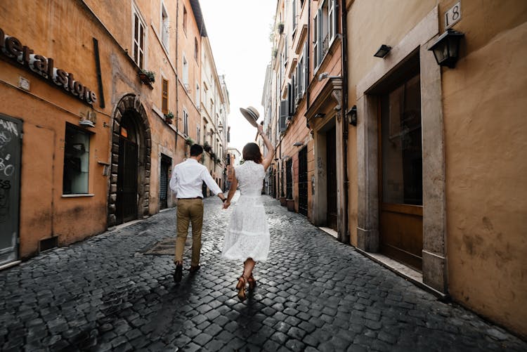 Couple Walking Down The Cobblestone Street In City 