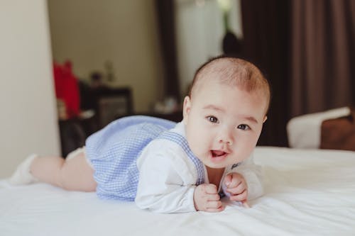 Baby Wearing Blue and White Clothing Lying on the Bed