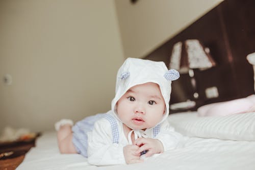 Charming Asian infant in cap lying on bed