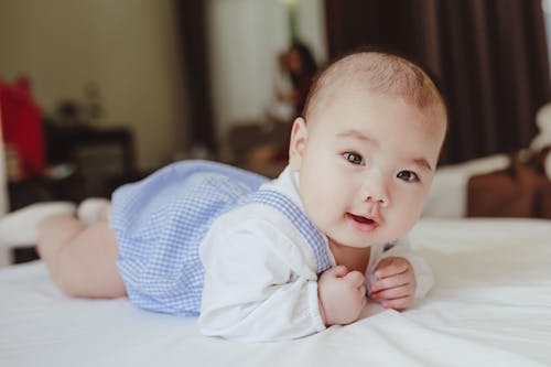 Free Adorable newborn baby in white cotton shirt and blue bodysuit lying on bed in light room Stock Photo
