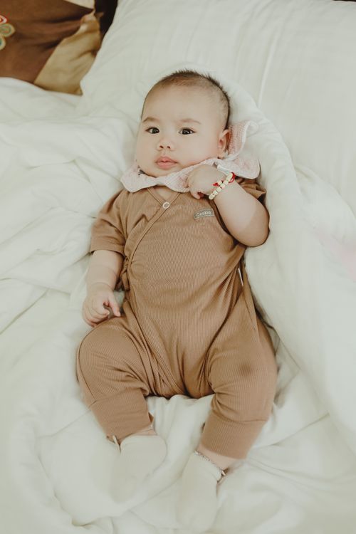 Free From above charming baby in beige bodysuit lying on white soft blanket on bed in daylight Stock Photo