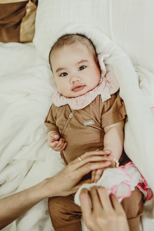 Free From above of female hand touching adorable little baby in bodysuit lying on comfortable blanket on bed Stock Photo