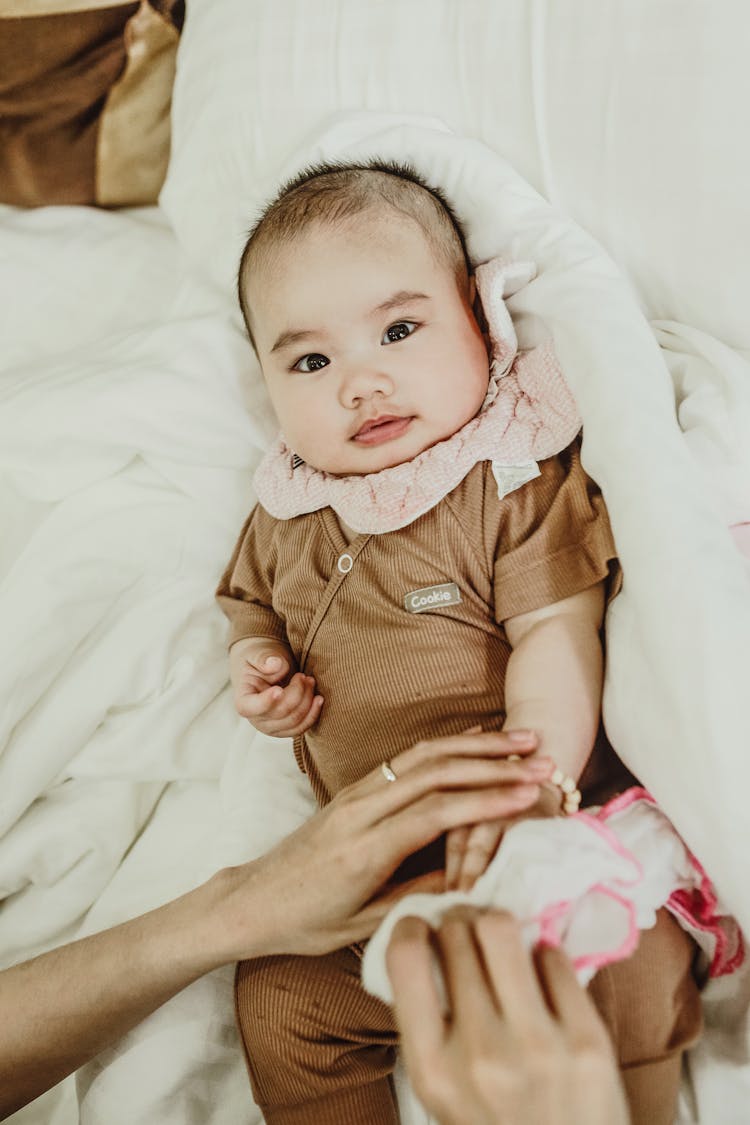 Female Hand Touching Newborn Lying On White Blanket