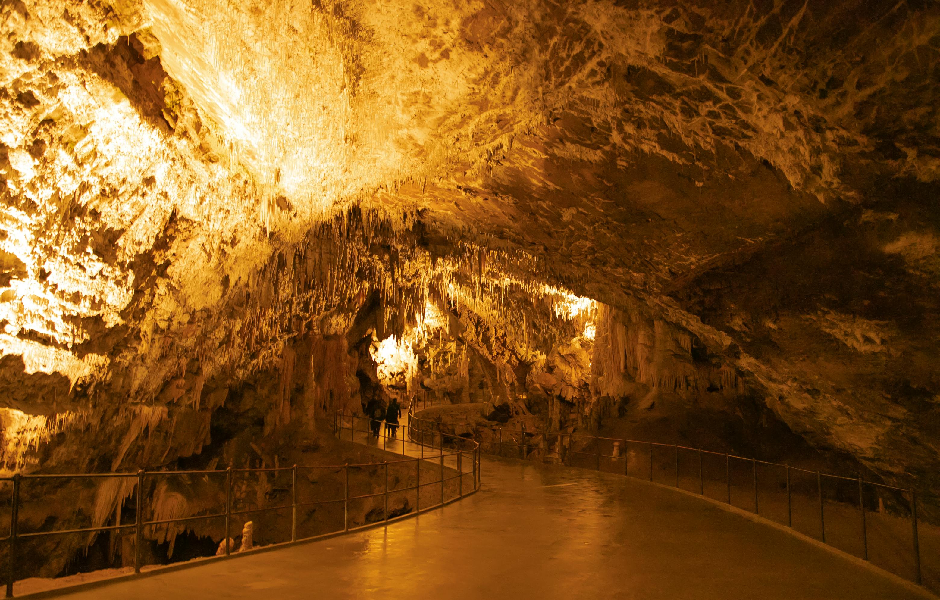 Illuminated limestone cave with stalactites and a paved walkway winding through the cavern