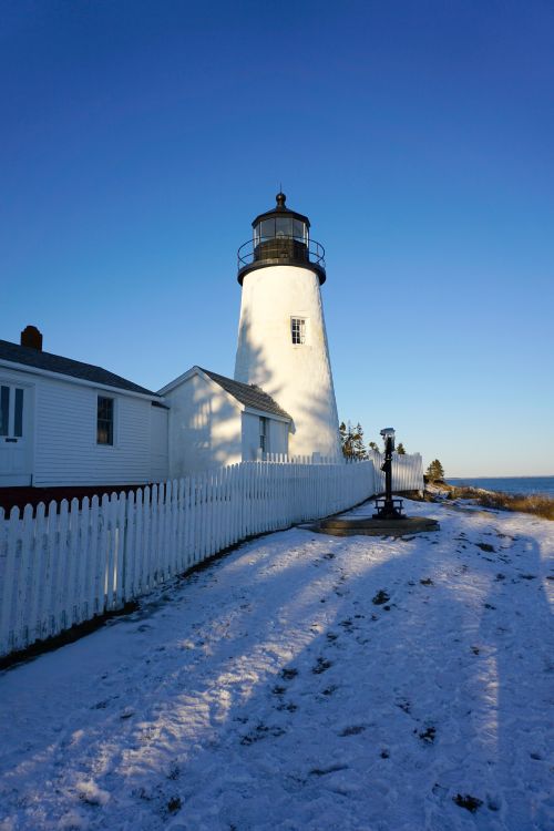 Free A picturesque lighthouse surrounded by snow on a clear winter day. Stock Photo