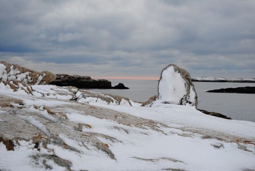 Free A serene snow-covered rocky coastline with ocean view during winter sunrise. Stock Photo