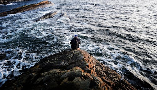 Photography of Person Sitting on Rock Near Ocean