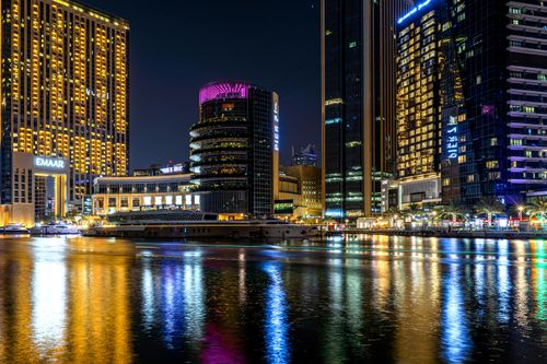Free Illuminated high-rise buildings reflecting off Dubai's waterfront at night. A vibrant cityscape showcasing urban elegance. Stock Photo