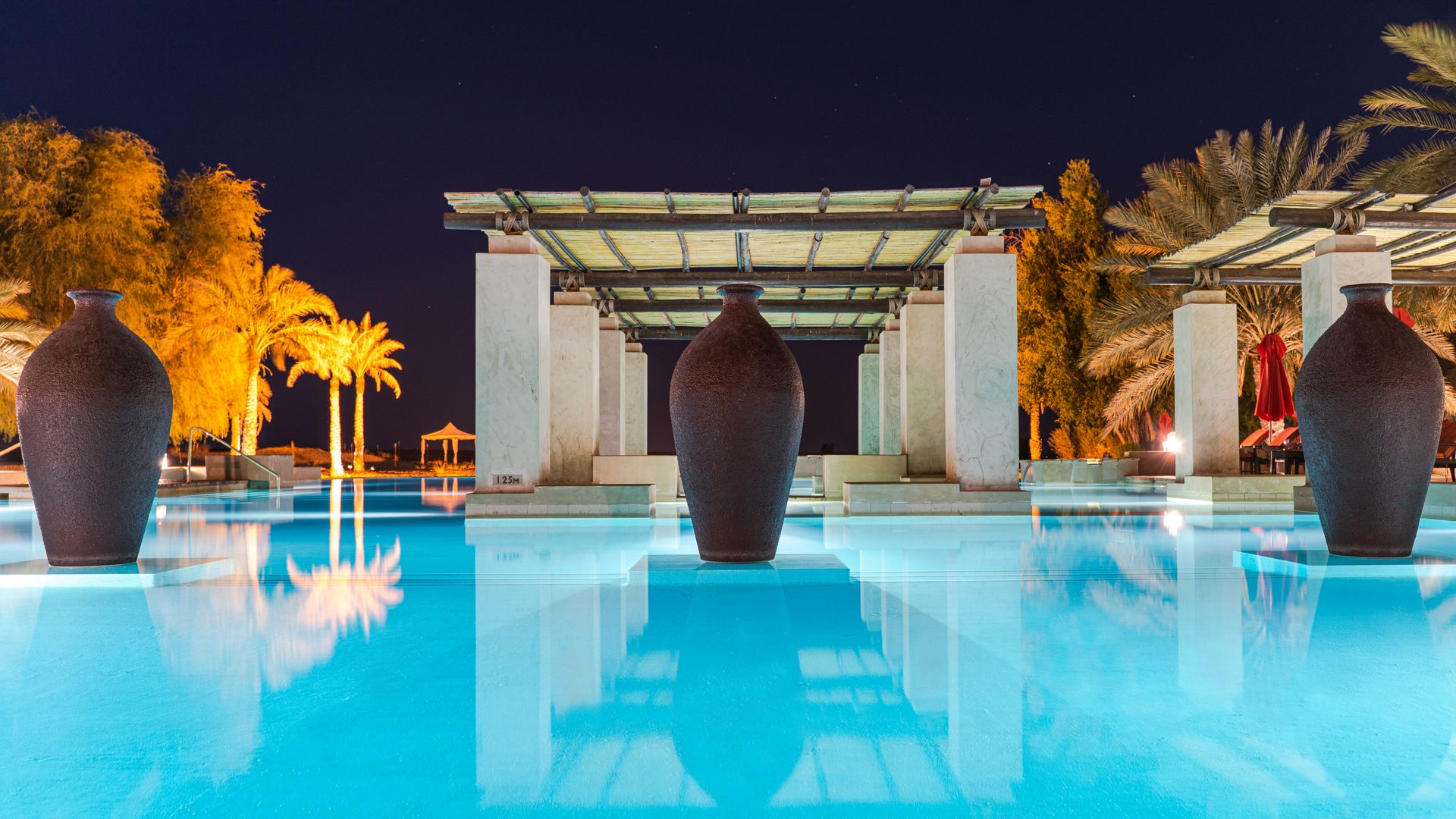 Stunning night view of a luxurious resort pool in Dubai, featuring elegant architecture and palm trees.
