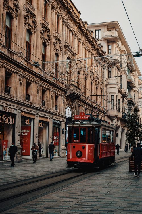 Free A vintage red tram travels down a lively urban street lined with historic architecture amidst bustling pedestrians. Stock Photo