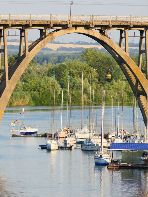 Free Serene view of sailboats docked under a large arched bridge on a sunny day in summer. Stock Photo