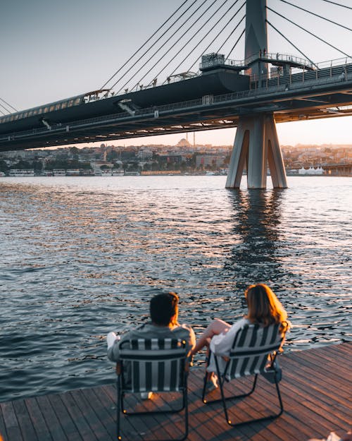 Free Couple Sitting on Chairs over a Platform Near the Bridge Stock Photo