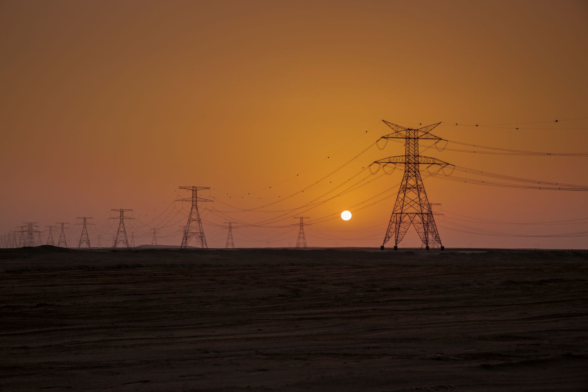 Sunset view of power lines in the Abu Dhabi desert, underscoring how Gulf compute ambitions depend on resilient electricity infrastructure.