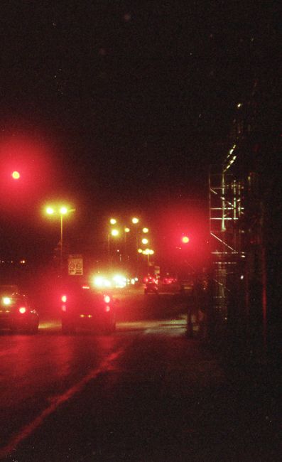 Atmospheric nighttime city street with car lights and traffic signals illuminating the road.