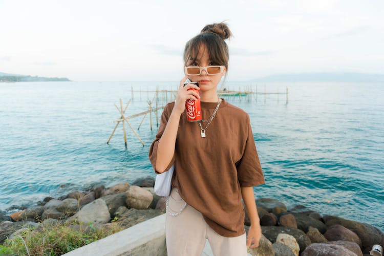 A Woman In Brown Shirt Holding A Can Of Soda