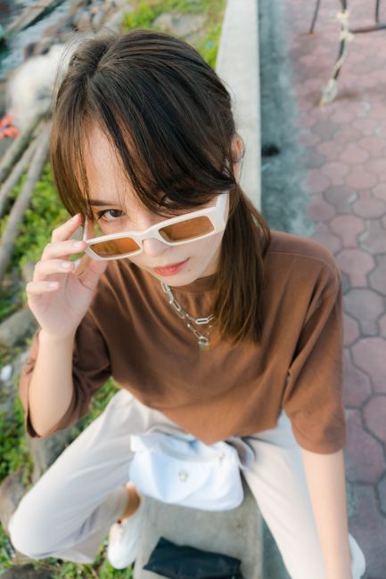 A fashionable young woman striking a pose outdoors with bold sunglasses.