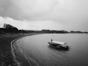 一张单色图像中，多云天空下岸边停着一艘孤独的渔船