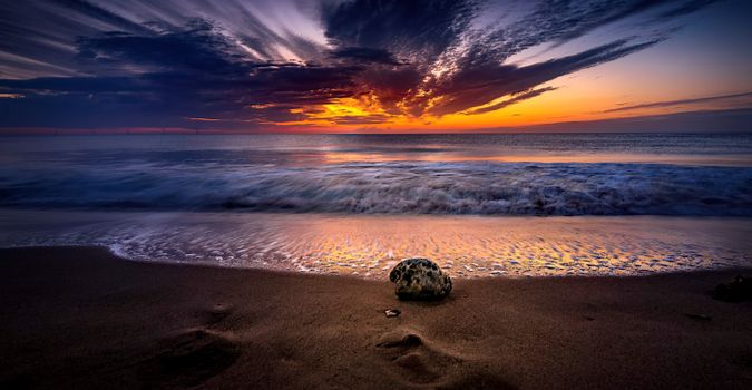 A stunning sunset over a sandy beach with waves crashing gently.