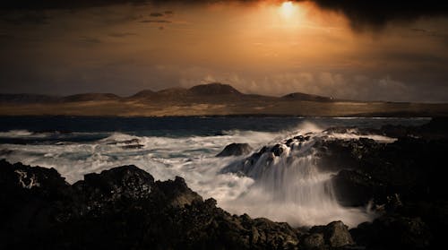 Free Ocean Waves Crashing on a Rocky Seashore during Sunset Stock Photo