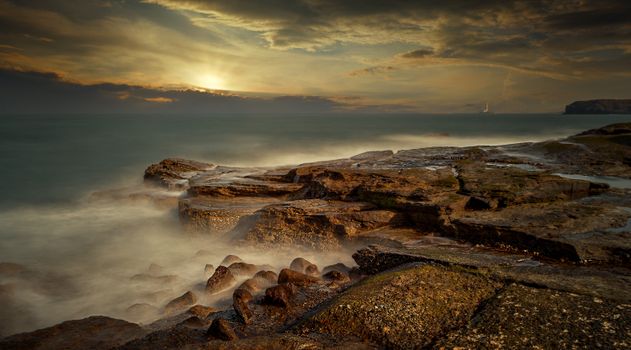 Breathtaking sunset view over a rocky seashore with waves crashing against the rocks, creating a mystical seascape.