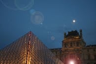 在巴黎多云的天空和满月的映衬下，夜间卢浮宫金字塔的戏剧性景色被照亮