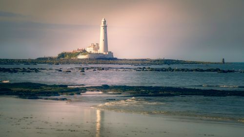 Free Peaceful scene of a lighthouse on a rocky beach at dawn, reflecting tranquility. Stock Photo