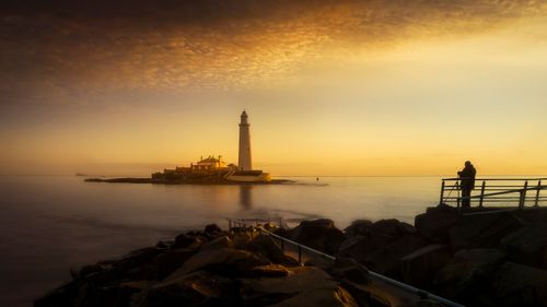 Free Captivating long exposure shot of a lighthouse at golden hour with a lone photographer by the sea. Stock Photo