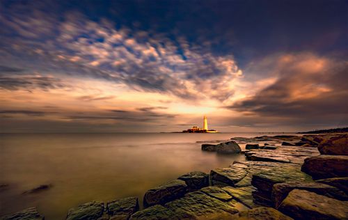 Free Beautiful long exposure shot of a lighthouse at sunset with rocky shore and dramatic clouds. Stock Photo