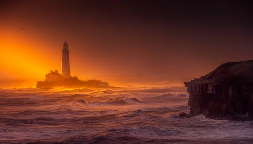 Free Captivating sunset over St Mary's Lighthouse with crashing waves and a vibrant sky. Stock Photo