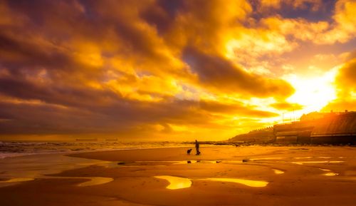 Free Silhouetted figure with a dog on a beach at sunset under a vibrant, dramatic sky. Stock Photo