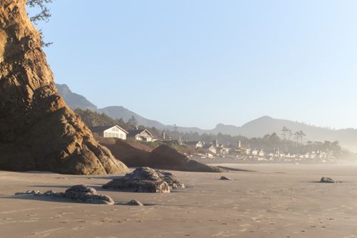 Free Serene beachfront at dusk with rocky formations and charming coastal houses. Stock Photo