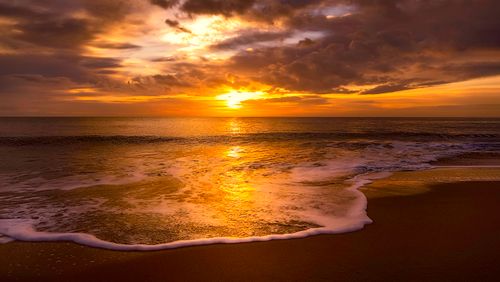 Free Golden sunset reflecting on the ocean waves and sandy beach with dramatic clouds. Stock Photo